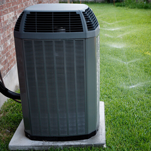 Modern air conditioner on backyard with working sprinkler system